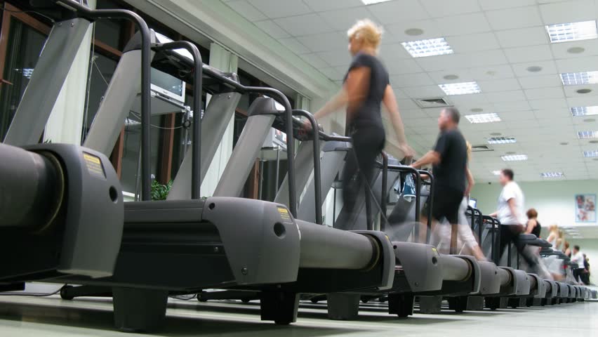 People on treadmills at fitness club. Machine provides a moving platform with a wide conveyor belt and an electric motor.