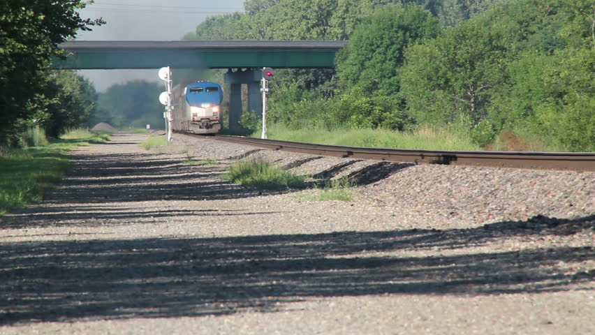 Passenger Train coming down the tracks to a crossing. Horn blowing.