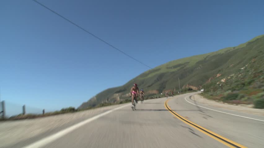 A group of bicyclists coast down winding coastal highway in California.