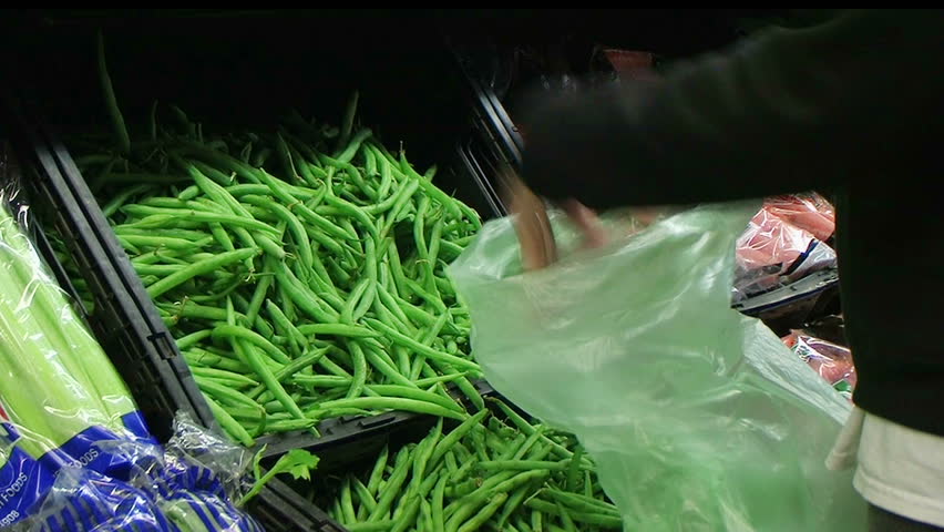 Woman selecting fresh green beans in grocery store produce department.