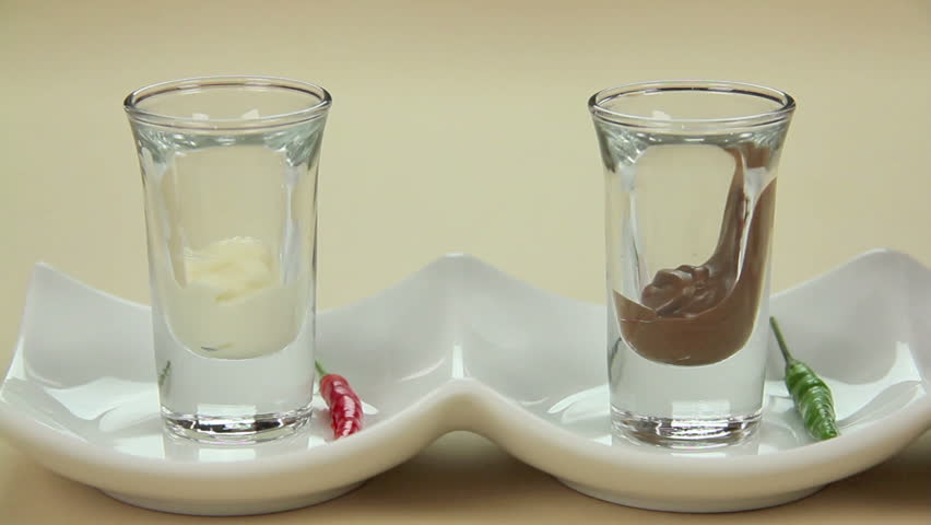 Putting fresh chillies into melted chocolate in a row of shot glasses.