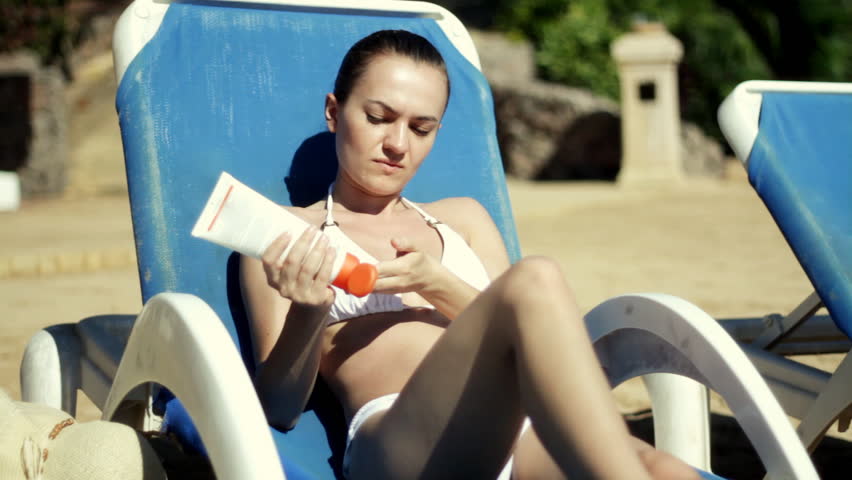 Attractive woman in bikini on sunbed applying sunscreen lotion