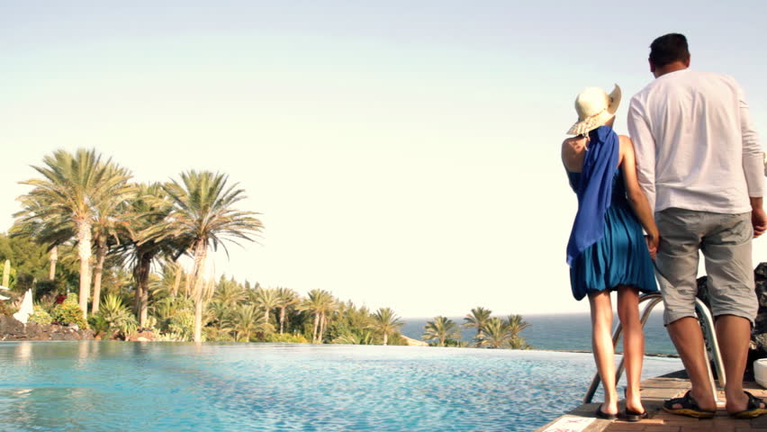 Couple standing and holding hands by the infinity pool