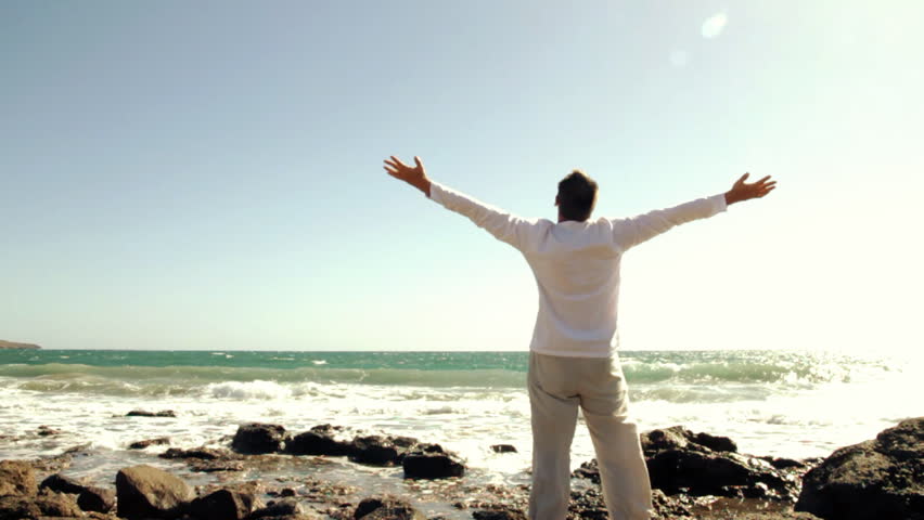 Man at the seashore raising hands to the sky, freedom concept