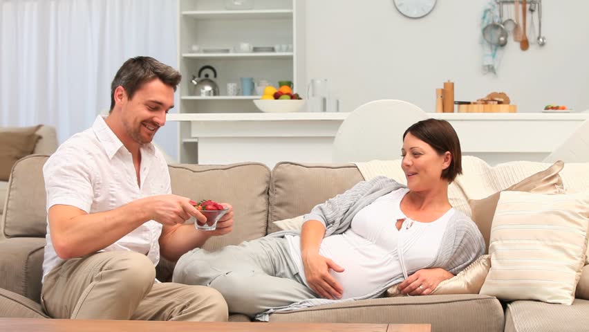 Man giving strawberries to his pregnant wife in the living room