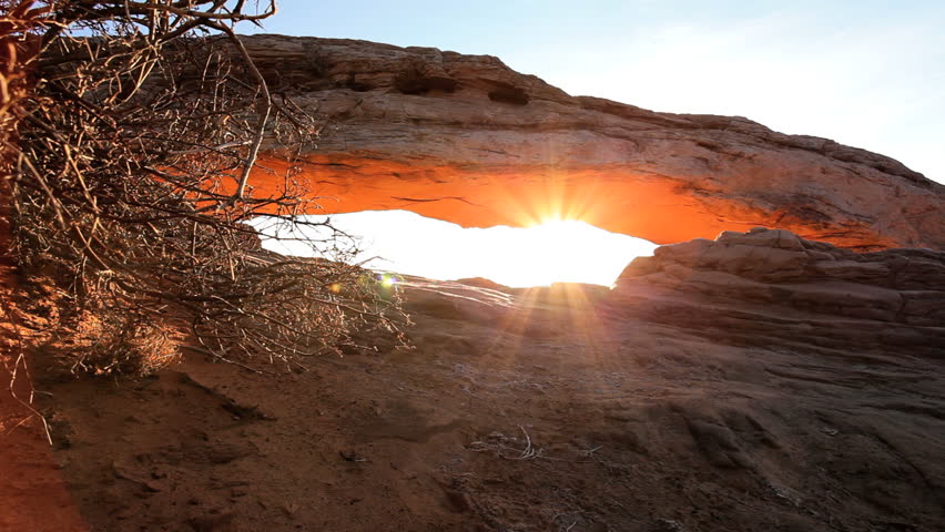 Panoramic view of a desert landscape through the sunrise hitting the sandstone Mesa Arch in Utah