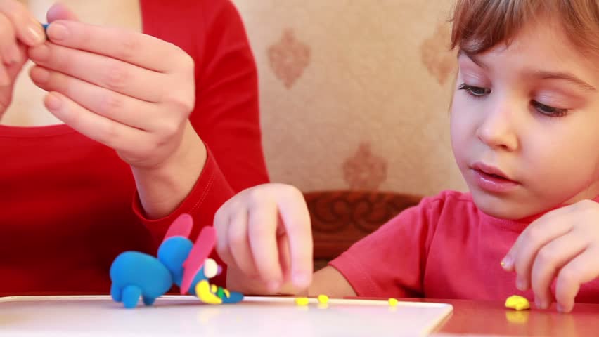 girl sculpts plasticine on table, watch with interest 
