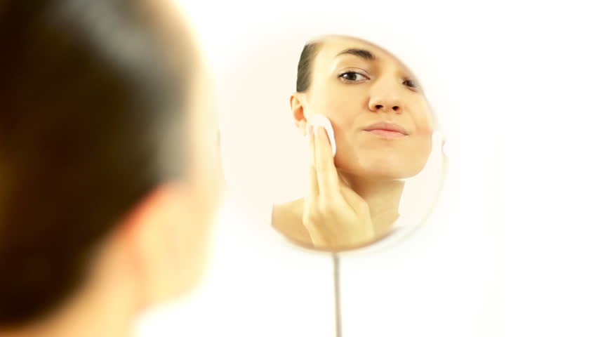 Woman cleaning face with cotton swab in the mirror