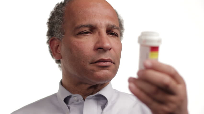 Mature man reading prescription bottle, on white