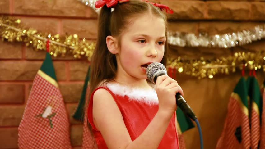 girl sings Christmas song into microphone in front of fireplace