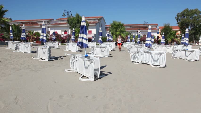 Young woman running closer by sand between lot of deckchairs