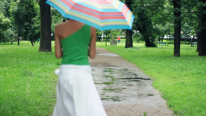 Woman with colorful umbrella jumping over the puddles, slow motion