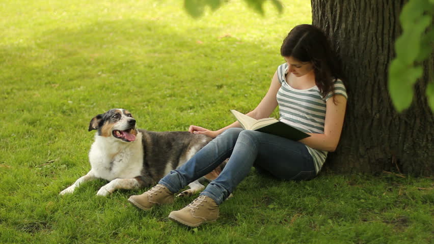 Teenager reads while petting dog.