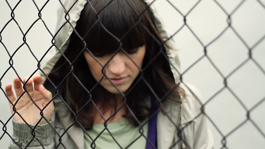 Sad woman behind chain-link fence, outdoors, slow motion
