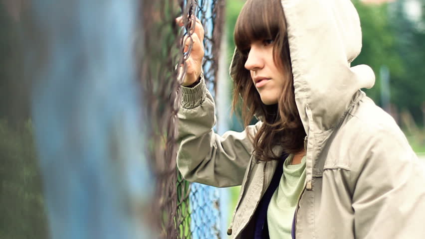 Sad beautiful woman by chain-link fence, outdoors 