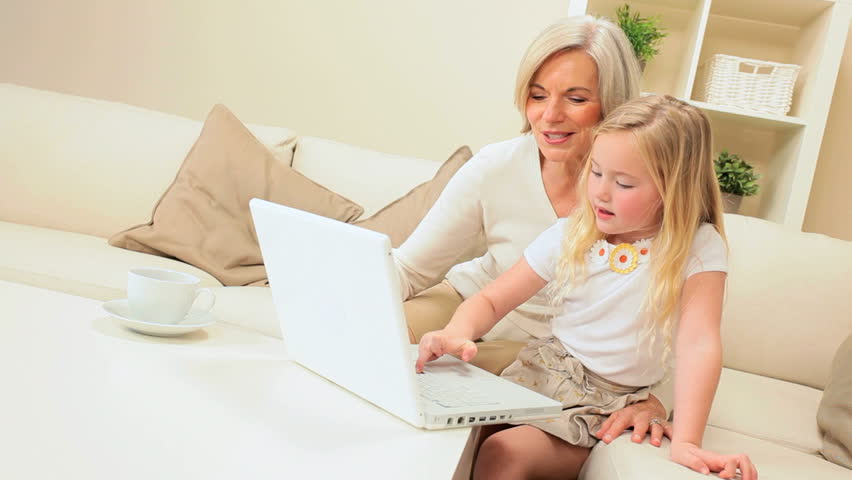 Pretty little blonde girl using a laptop at home with grandma proudly watching