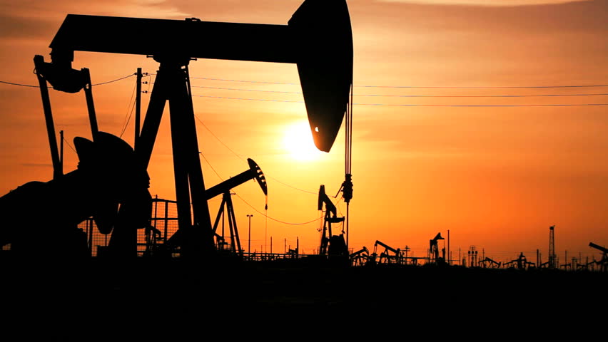 Oil donkeys in perpetual motion producing crude oil in a desert location at sunset