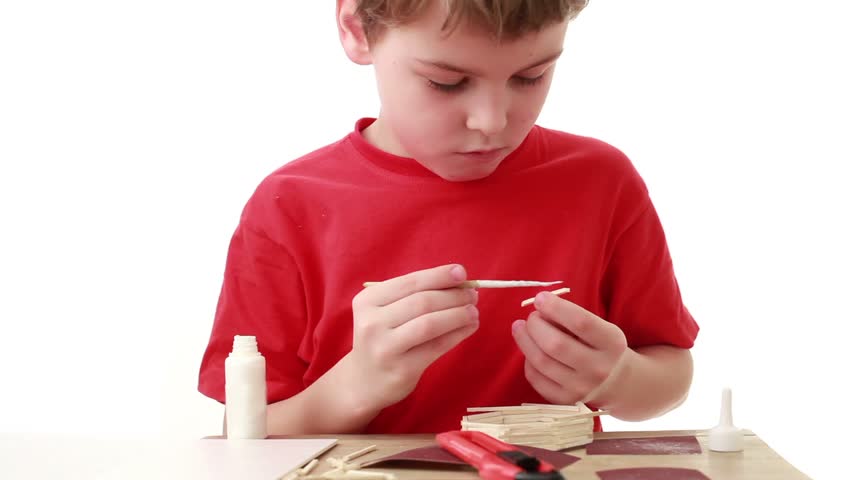 Boy put adhesive to the match, in front of him on the table unfinished house from matches