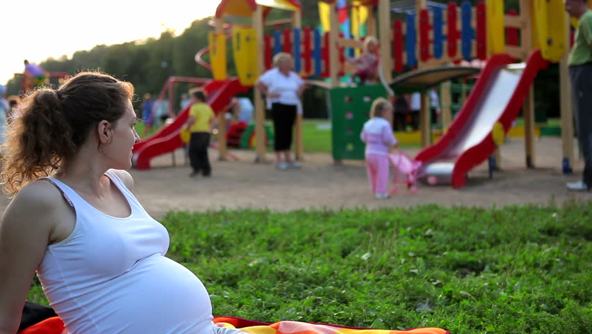 Pregnant woman looks at the children on the playground