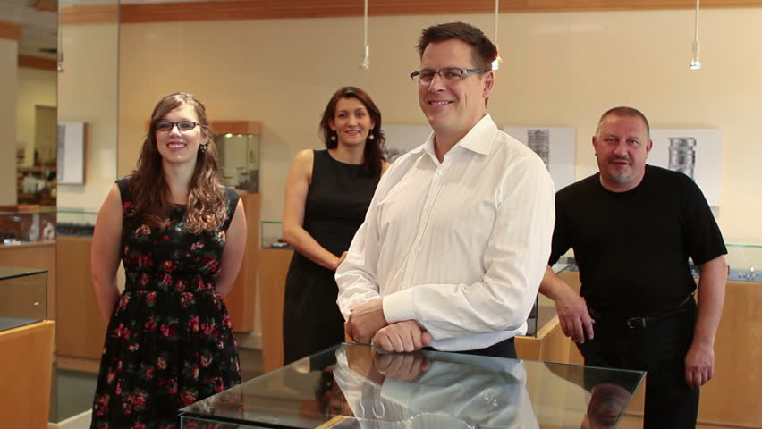 Jewelry store owner standing with employees in his store, dolly shot