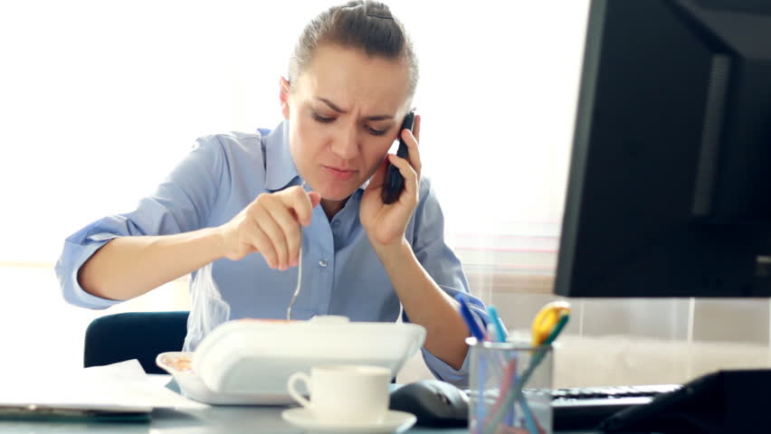 Businesswoman eating lunch in the office while talking on mobile phone