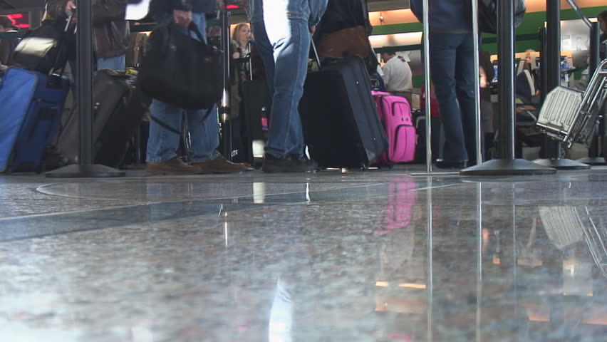 Airline passengers queue up in line to check in baggage at ticket counter at busy airport; good audio