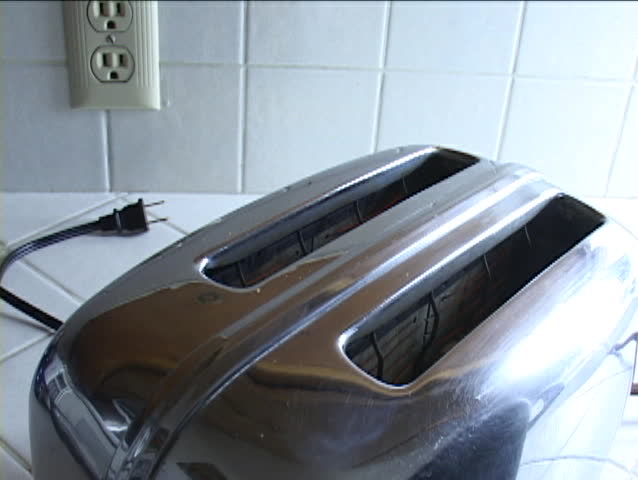 Smoke rises from an unplugged toaster as two pieces of burnt toast pop up.