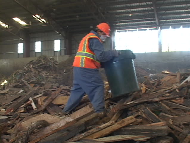 A recycling plant worker places scraps into a garbage can.