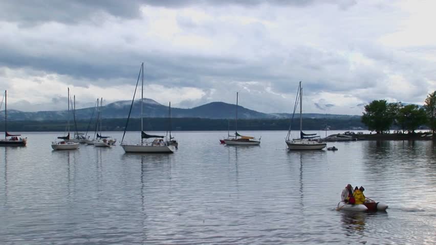 Clouds cover a mountain range in the distance of sailboats on calm water at Lake Champlain in Vermont.