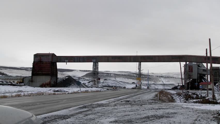 Pan across an old abandoned mine in winter with traffic passing on a road.