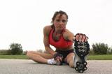 A pretty brunette in fitness wear, with remarkable muscle definition, stretches prior to jogging outdoors.  Low angle.