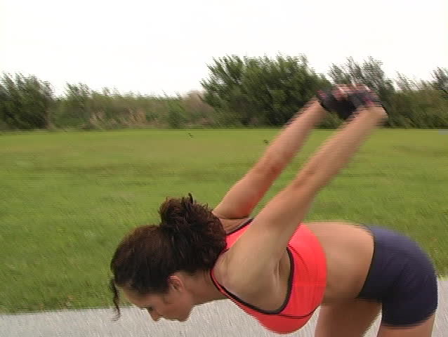 A pretty brunette in fitness wear, with remarkable muscle definition, stretches prior to jogging outdoors.  Camera mounted on fig rig; deliberate movement.