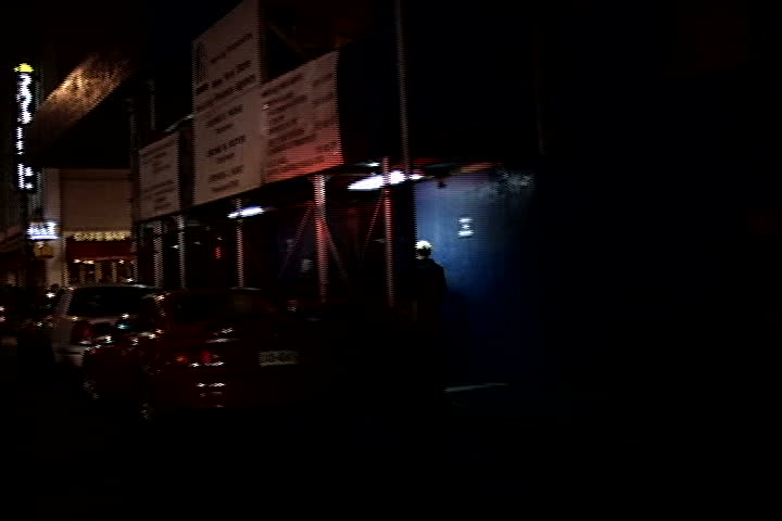 city night footage of cop car on a street corner with sirens on.