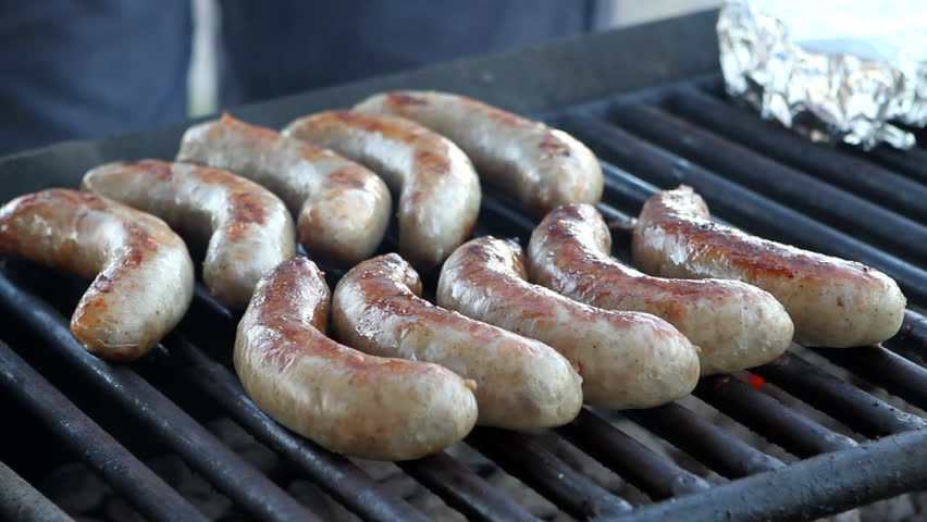 Metal tongs are used to turn bratwurst sausages as they cook over a charcoal grill.