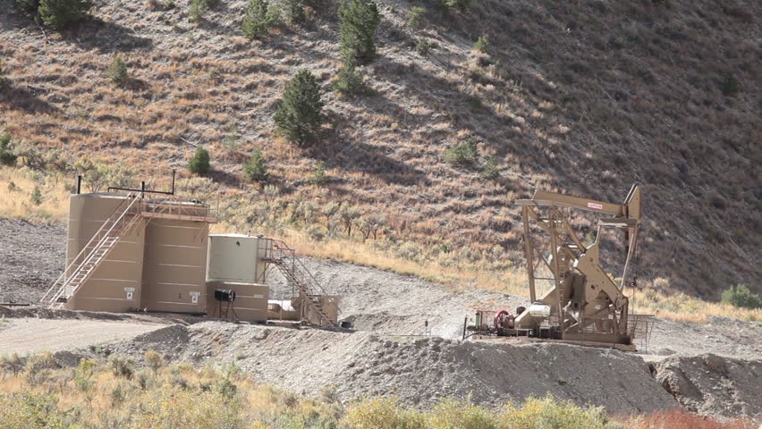 Oil well pumping crude from deep desert valley between mountains in central Utah. Propane motor powers the pump that extracts the oil. Fast motion.