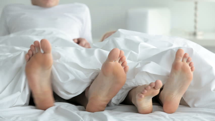 Feet of playful couple on bed stuck out of blanket 