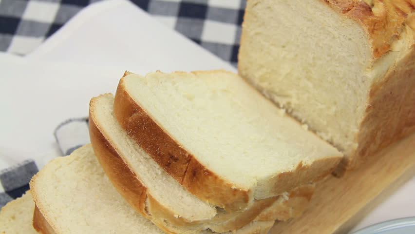 Bread being sliced then buttered with butter. 