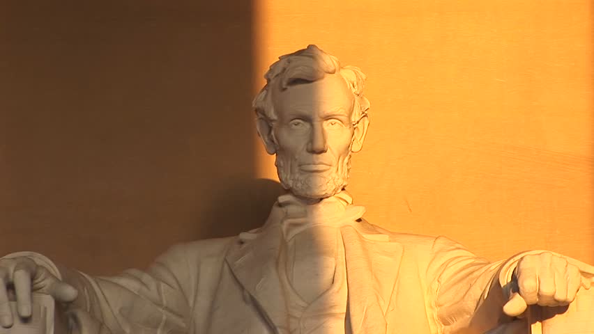 President Lincoln's sculpted face is seen half in shadow, the other half bathed in golden light.