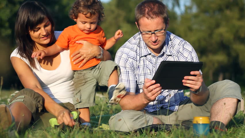Happy family with tablet computer in the park, dolly shot 