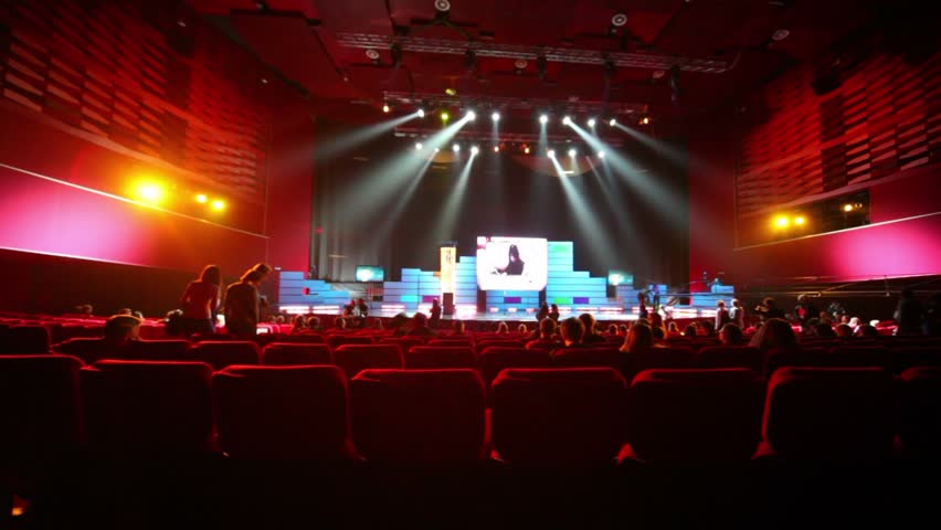 Big auditorium with red seats, illuminated scene, people in auditorium 