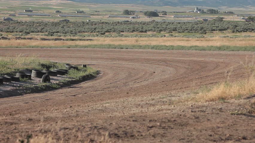 Race trucks on dirt oval course away from view. Highly modified stock cars driving and racing on a very dirty and dusty track corner. High speed and dusty.