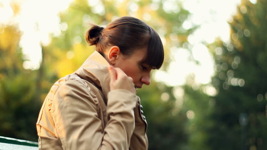 Sick woman sitting on park bench and coughing