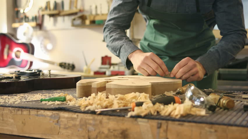 man working as artisan in italian workshop with guitars and musical instruments, smoothing guitar body