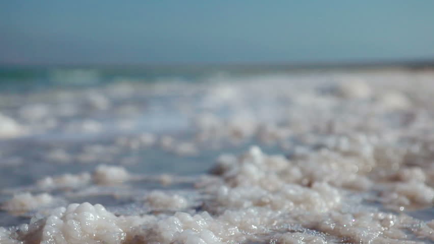 Low angle of the water lapping over the salt deposits on the shore of the Dead Sea in Israel.  The shot racks focus from the foreground to the background.