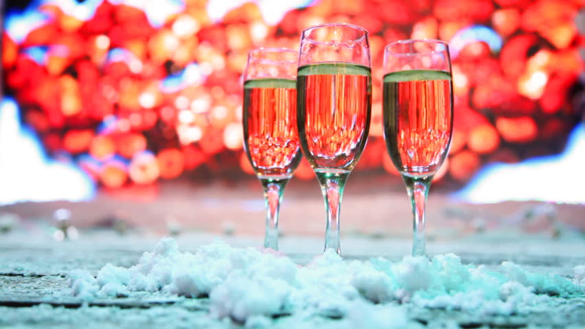 three glasses champagne or white wine stand sprinkled snow on background of festive lights flashing