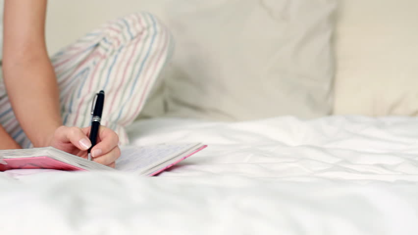Young woman writing diary while sitting on the bed, dolly shot