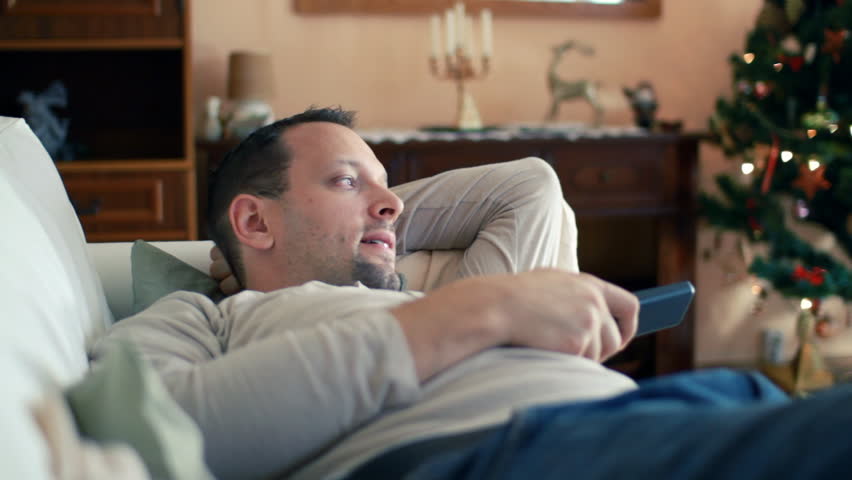Young man with tv remote watching tv on sofa 