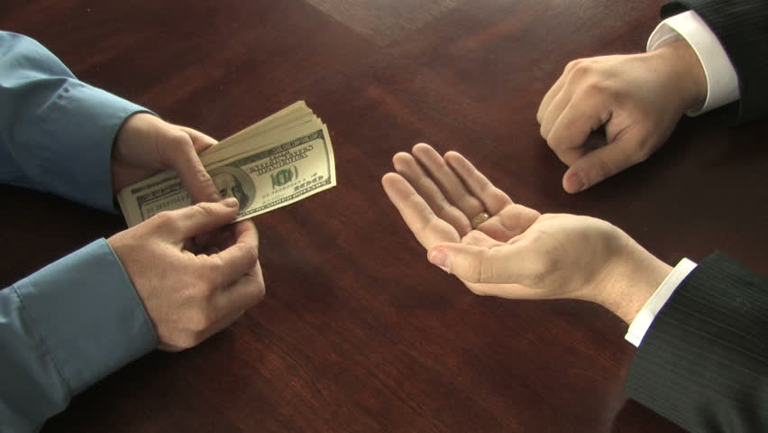 A man counts out hundred dollar bills into the hand of another businessman, who takes the money 