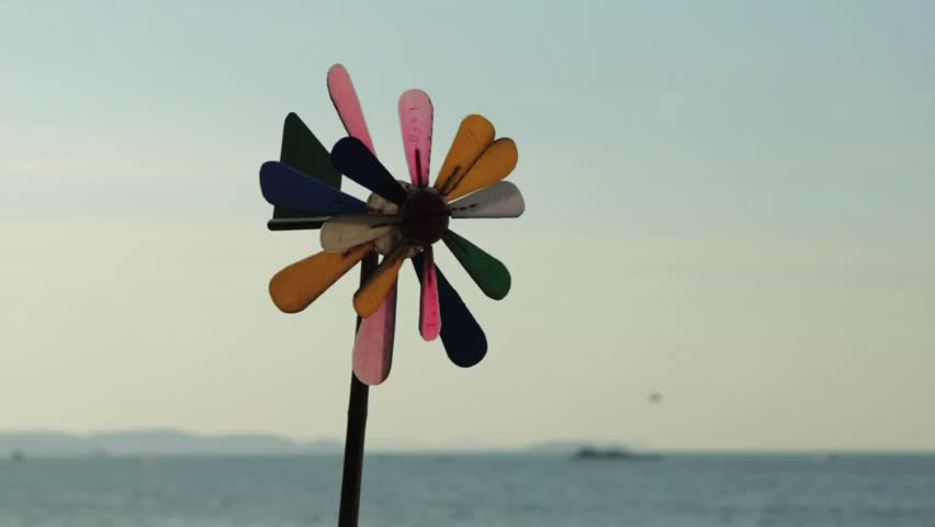 a beach pinwheel blowing and spinning in the beach breeze with a parasailer in the distance.