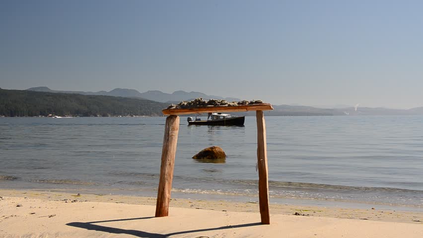 small boat crossing in front of sandy ocean beach with stone and wooden gate at sunny day in Vancouver, Canada.